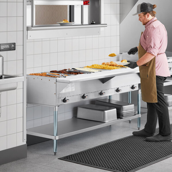 A man in a commercial kitchen using a ServIt liquid propane steam table.