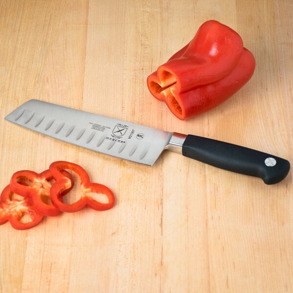 A Mercer Culinary Genesis Forged Nakiri Knife with sliced red bell peppers on a cutting board.