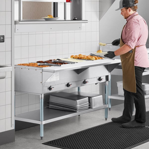 A man in a brown apron using a ServIt liquid propane steam table in a kitchen.