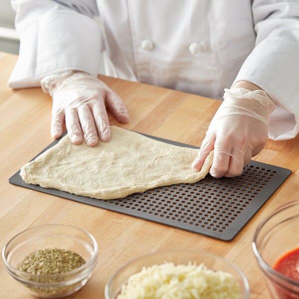 A person in plastic gloves using an American Metalcraft Hard Coat Anodized Aluminum Mega Flatbread Screen to make pizza dough.
