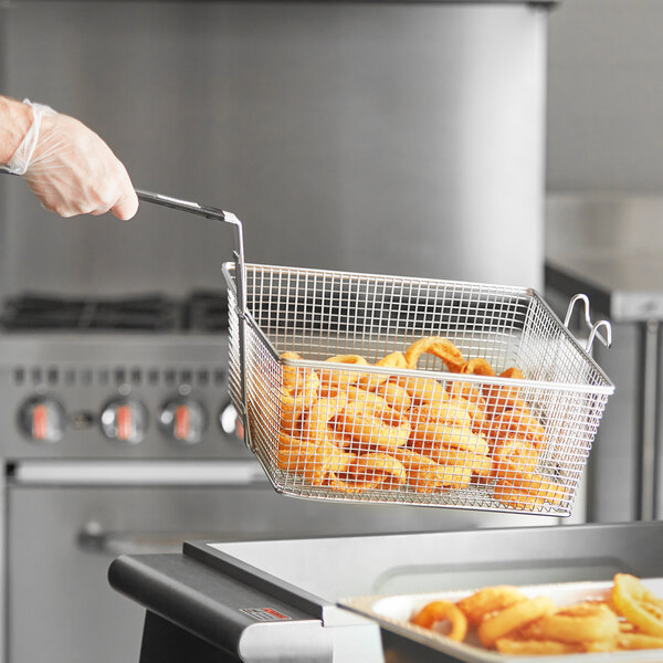 A hand holding a Pitco fryer basket full of food.