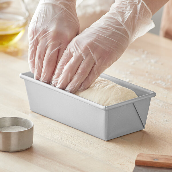 A person in gloves using a Baker's Mark aluminized steel loaf pan to make bread