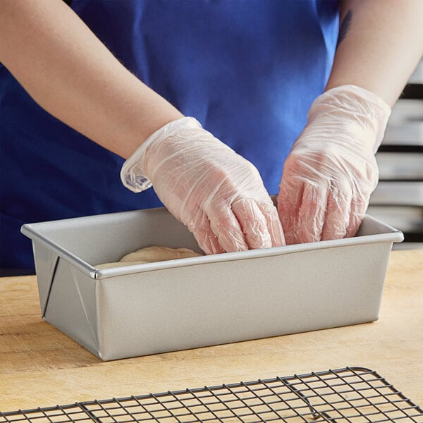 A person wearing gloves putting dough into a Baker's Mark bread loaf pan.