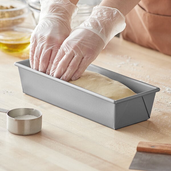 A person in gloves using a Baker's Mark aluminized steel bread loaf pan to make a loaf of bread.