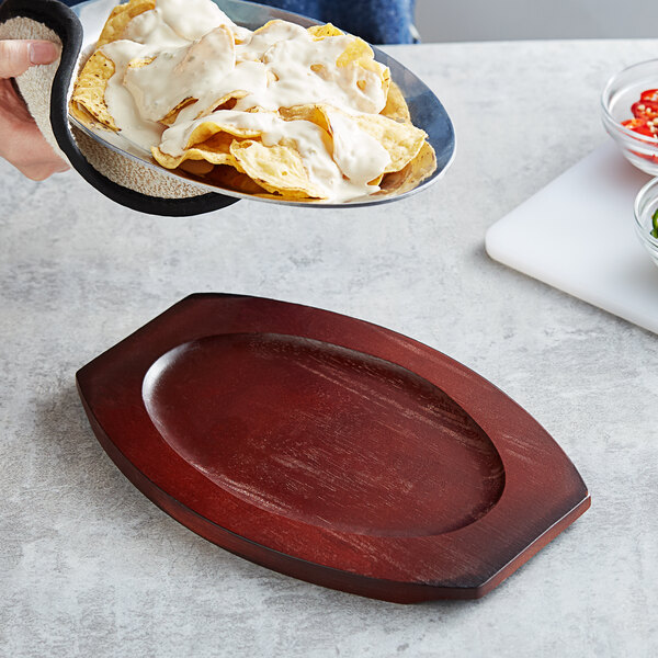 A person holding a Choice oval rubberwood underliner with a plate of chips and white sauce.