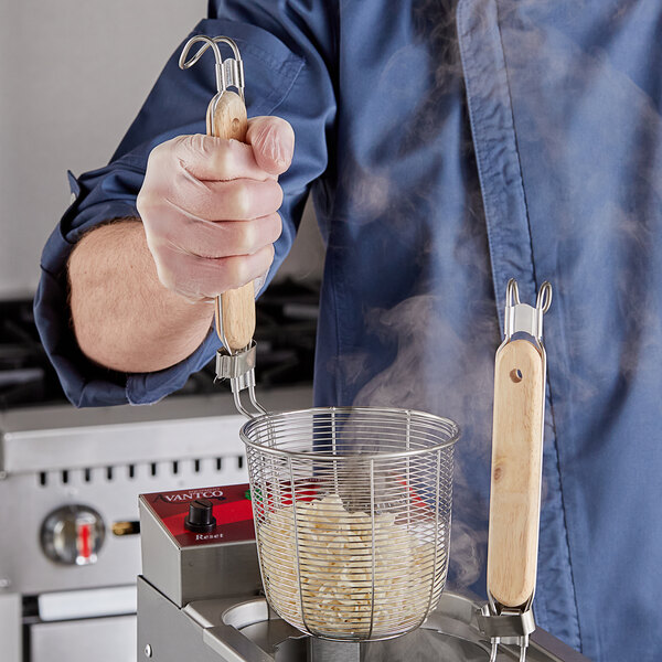 A man using an Avantco pasta basket with wooden handle to cook pasta.