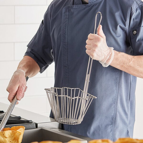 A man in a chef's uniform holding a Choice stainless steel wire basket filled with tortilla chips.