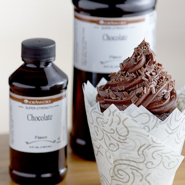 A chocolate cupcake in a wrapper next to a bottle of LorAnn Oils chocolate syrup.