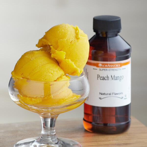 A glass with yellow ice cream next to a bottle of LorAnn Peach Mango flavor syrup.