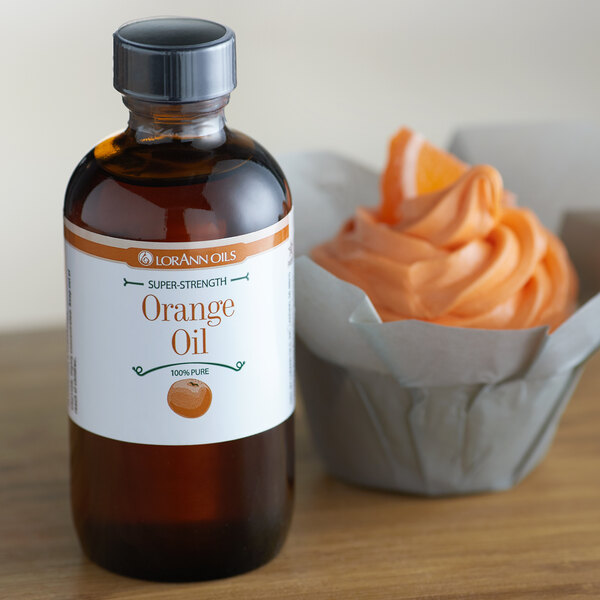 A bottle of LorAnn Oils All-Natural Orange Super Strength Flavor next to a cupcake with orange frosting.