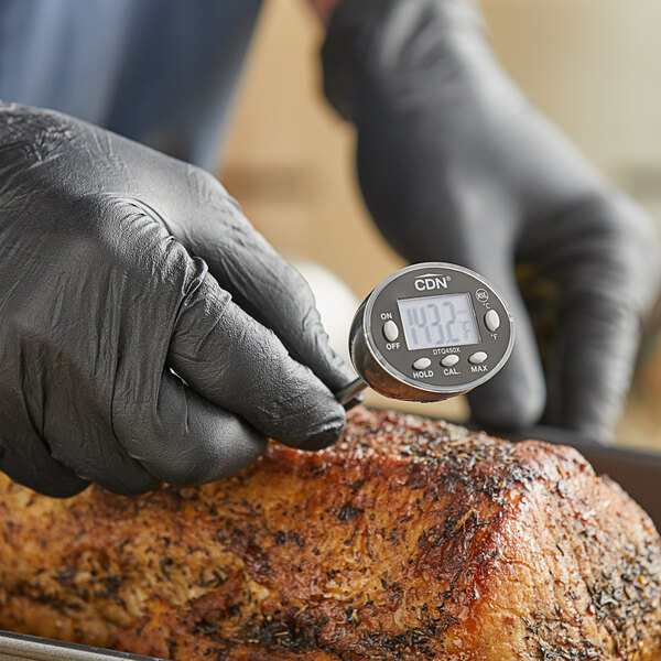 A person wearing a black glove using a CDN digital pocket probe thermometer to check the temperature of a piece of meat.