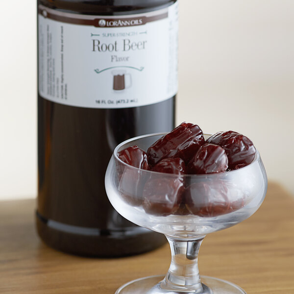 A glass of red dates in front of a brown bottle of LorAnn Oils Root Beer Super Strength Flavor.