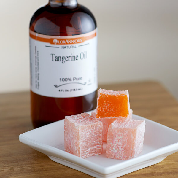 A bottle of LorAnn Oils Tangerine Flavor next to cubes of orange food on a plate.