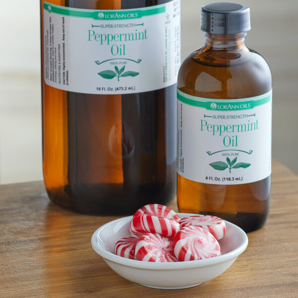 A bowl of red and white striped peppermint candy on a table with a bottle of LorAnn Oils Peppermint Flavor next to it.