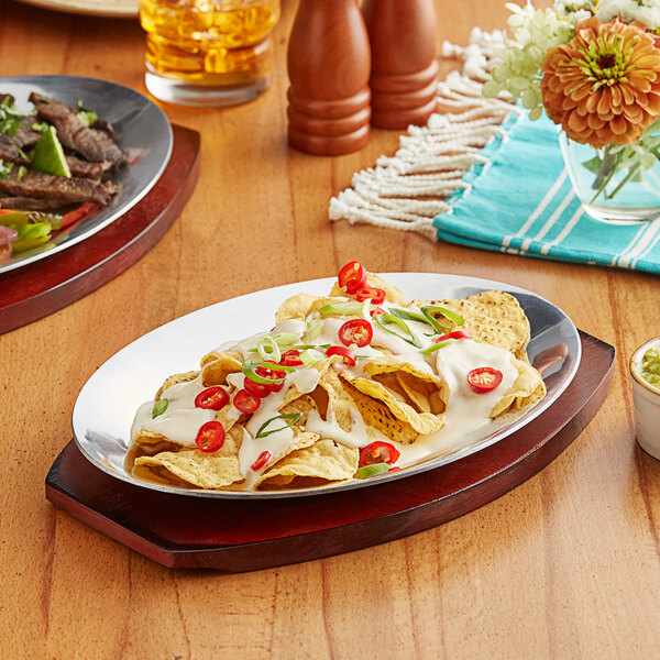 A table with a Choice oval aluminum sizzler platter with nachos, sauce, and meat on it.
