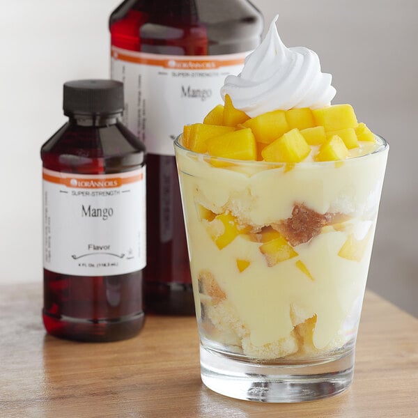 A glass of dessert with a white frosting and fruit in it next to a bottle of LorAnn Oils Mango Super Strength Flavor.