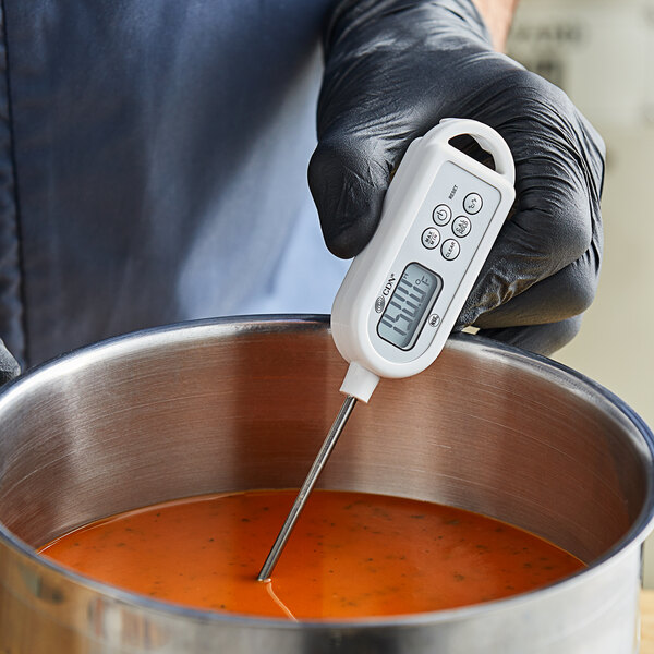 A hand in gloves holding a CDN ProAccurate digital pocket probe thermometer.