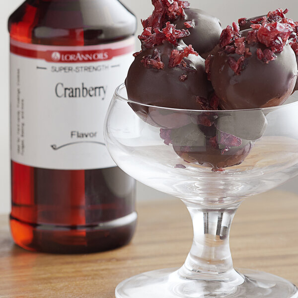 A glass bowl of chocolate truffles next to a bottle of LorAnn Cranberry Super Strength Flavor.
