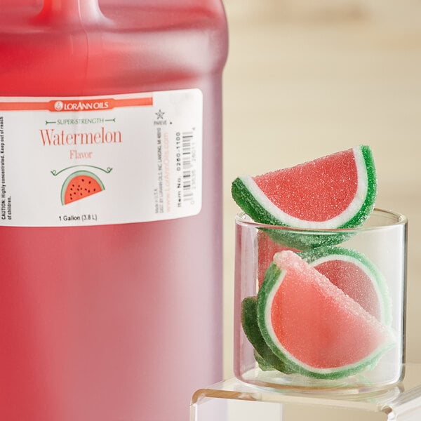 A jug of LorAnn Oils Watermelon Super Strength Flavor next to a glass of watermelon juice.