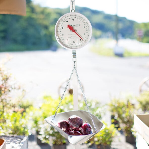 A Cardinal Detecto hanging scale with cherries in a metal scoop.
