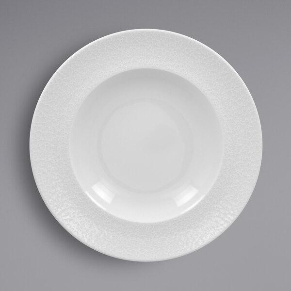 A close-up of a RAK Porcelain white plate with an embossed textured rim.