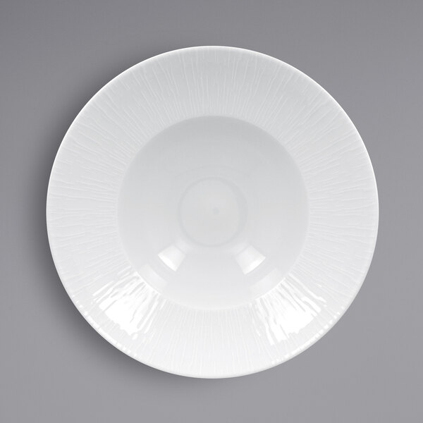 A close-up of a white RAK Porcelain Soul extra deep plate with an embossed pattern on the rim.