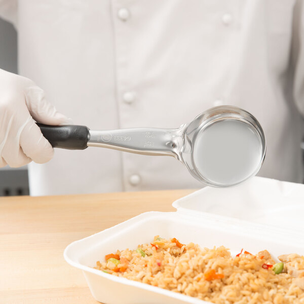 A person in white gloves using a Vollrath black round portion spoon to serve rice and vegetables from a white container.