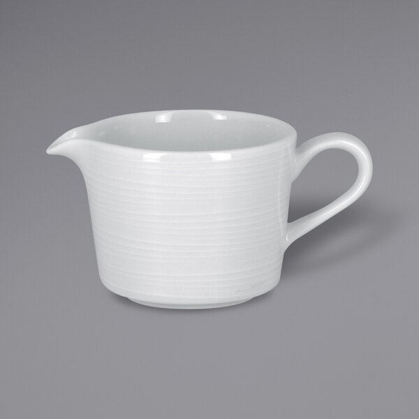 A white porcelain gravy boat with an embossed design and a handle.