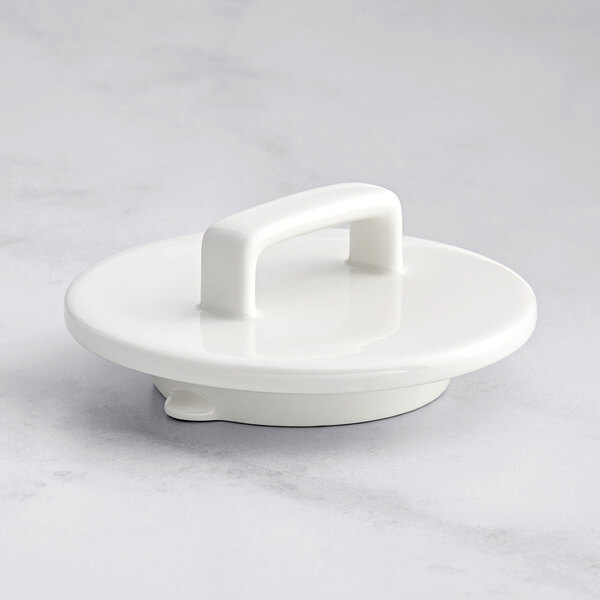 A RAK Porcelain warm white lid with a handle on a white table.