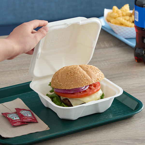 A hand holding a burger in a Fabri-Kal Greenware hinged container.