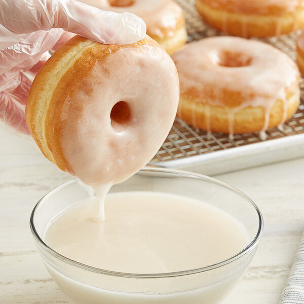 A hand holding a glazed doughnut over a bowl of milk.