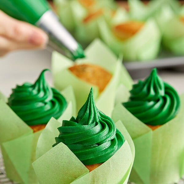 A hand using Rich's Green Buttrcreme icing to frost a cupcake.