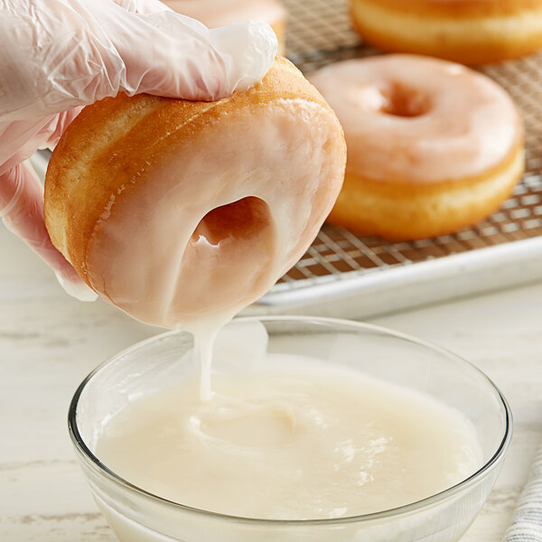 A hand dipping a Rich's glazed donut into a bowl of white liquid.