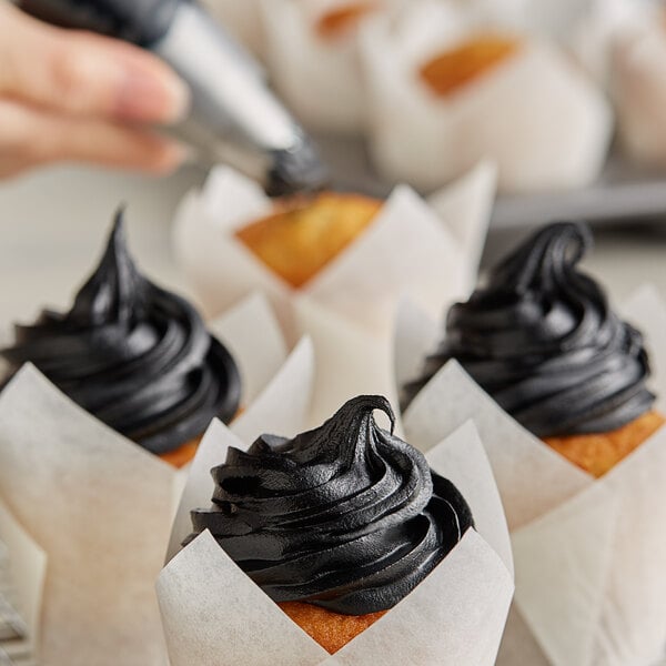 A person using Rich's Black Buttrcreme Icing to decorate cupcakes with black frosting.