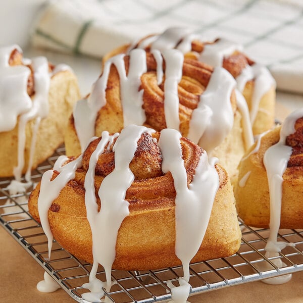 Cinnamon rolls with Rich's Classic White Donut & Roll Icing on a cooling rack.