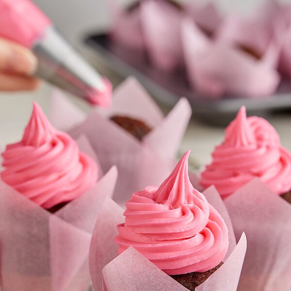 A person using Rich's Pink Buttrcreme Icing in a pastry bag to frost a cupcake.