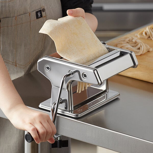 A woman using a Choice Prep stainless steel manual pasta machine to make pasta with a piece of dough.