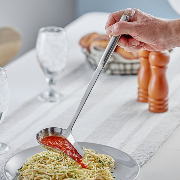 A hand holding a Choice stainless steel pour spout ladle full of spaghetti sauce.