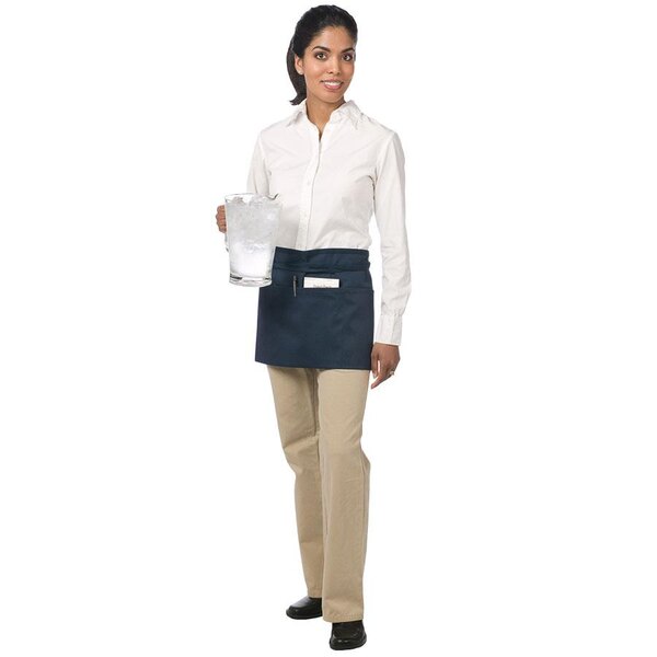 A woman wearing a navy blue Chef Revival waist apron with a pen in the pocket.