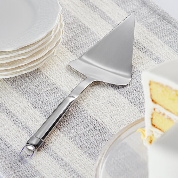 A stainless steel wide cake server with a hollow handle cutting a cake on a table.