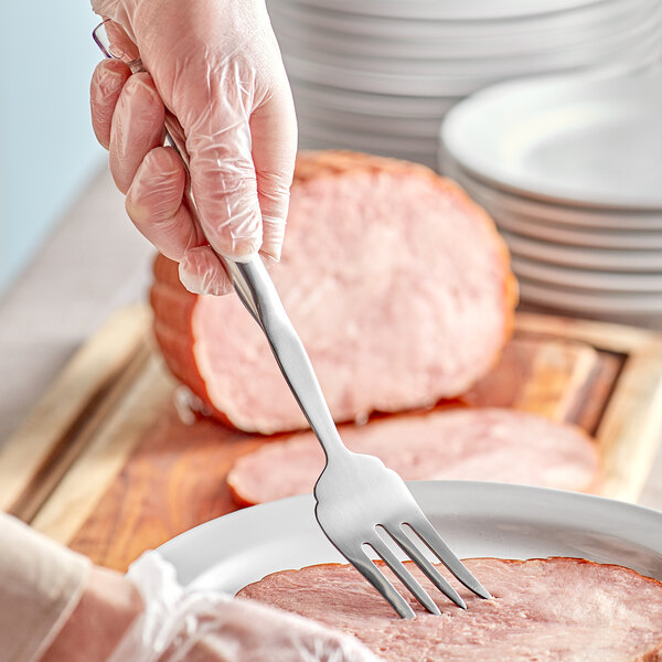 A hand holding a Choice stainless steel 4-tine pot fork over a plate of meat.