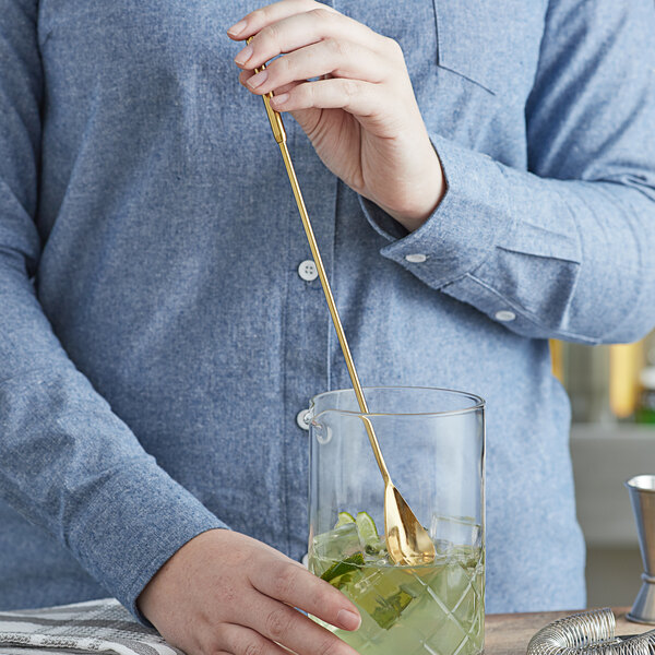 A person mixing a drink with a gold spoon.