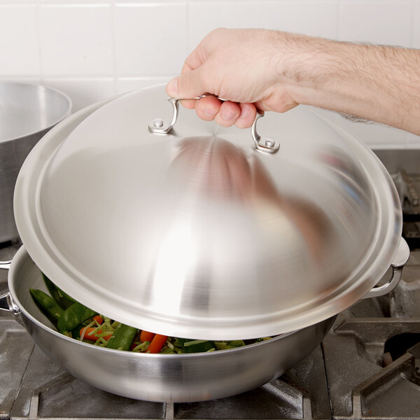 A hand using a Vollrath high domed lid to cover a pan of food.