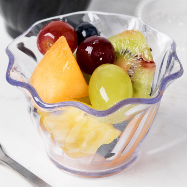 A table with a Cambro clear swirl bowl filled with fruit.