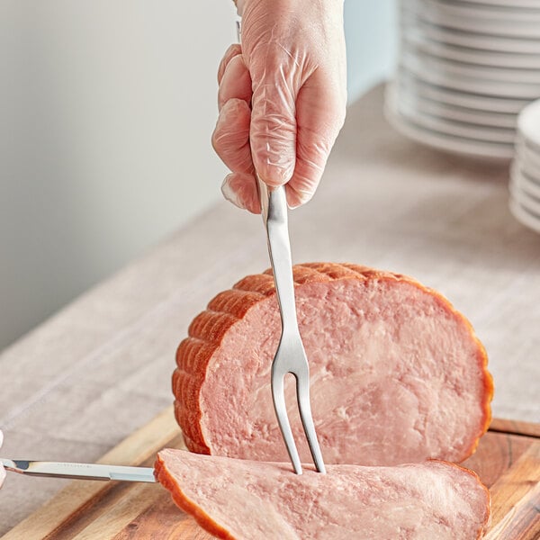 A person using a Choice stainless steel 2-tine pot fork to cut ham.