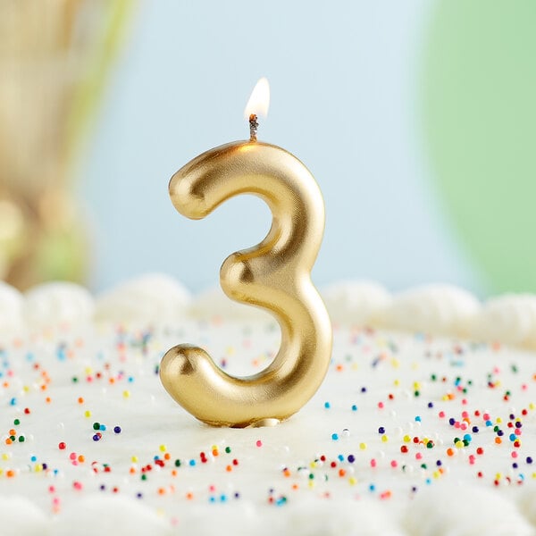 A gold "3" candle on a white cake.