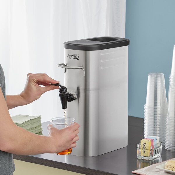 A woman using an Avantco iced tea dispenser to pour a drink.