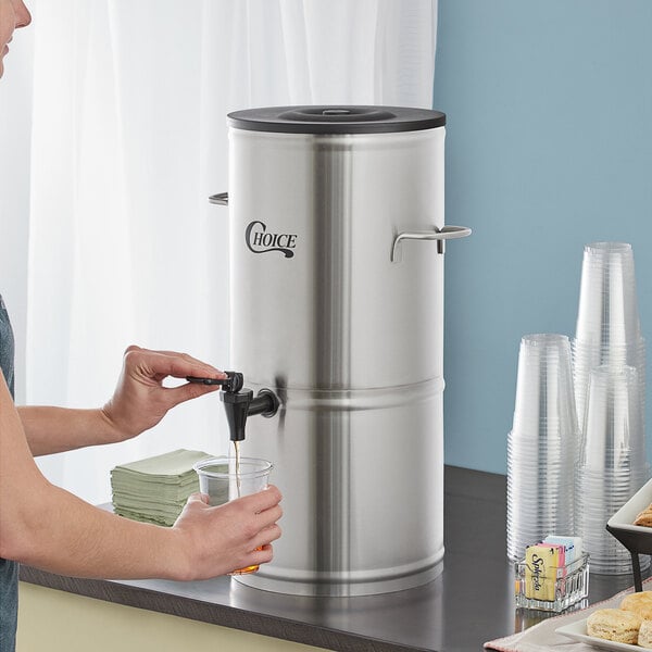 A woman pouring water from a faucet into a Choice 5 Gallon Iced Tea Dispenser.
