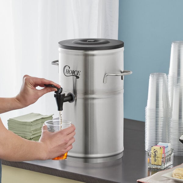 A person pouring a drink from a Choice 2 Gallon Round Iced Tea Dispenser tap into a glass.