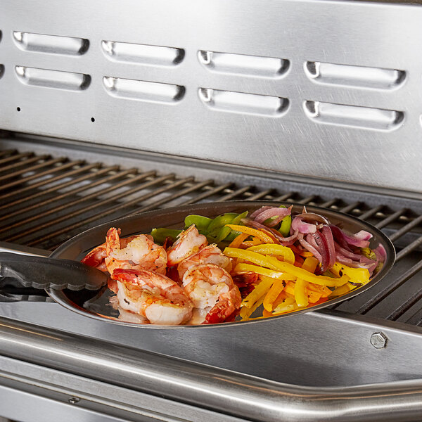 An oval stainless steel sizzler platter with shrimp and vegetables on a grill.
